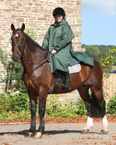 EQUIDRY women's long waterproof horse riding coat in black forest green/cream modelled by rider out hacking on horse showing storm skirts 