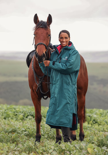 EQUIDRY women's long waterproof horse riding coat in Teal/Peacock Pink modelled by rider stood with horse 