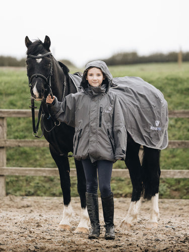 Shortie Child's Oversized Short Waterproof blouson style Riding Jacket Thin Fleece Lining Stowaway Hood in charcoal/grey girl with horse wearing matching exercise sheet